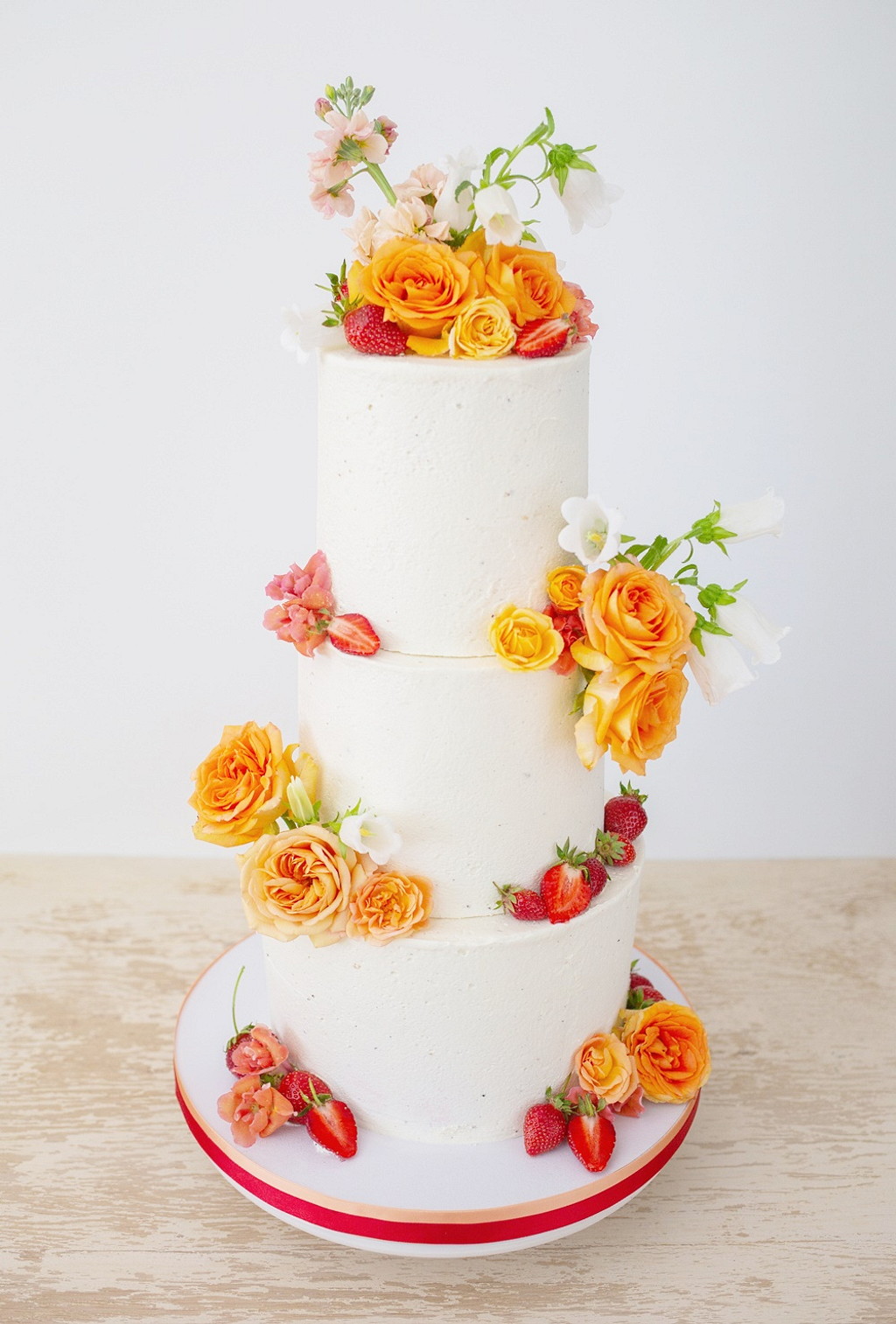 Dreist&ouml;ckige wei&szlig;e vegane Hochzeitstorte mit Bl&uuml;ten und Erdbeeren dekoriert